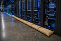 Liquid-cooled AI data center rack row with StormBag burlap flood barrier at the base
