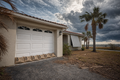 Properly-scaled StormBag burlap sandbags lined along a Florida home garage door under approaching hurricane storm clouds, with drought-stressed yard